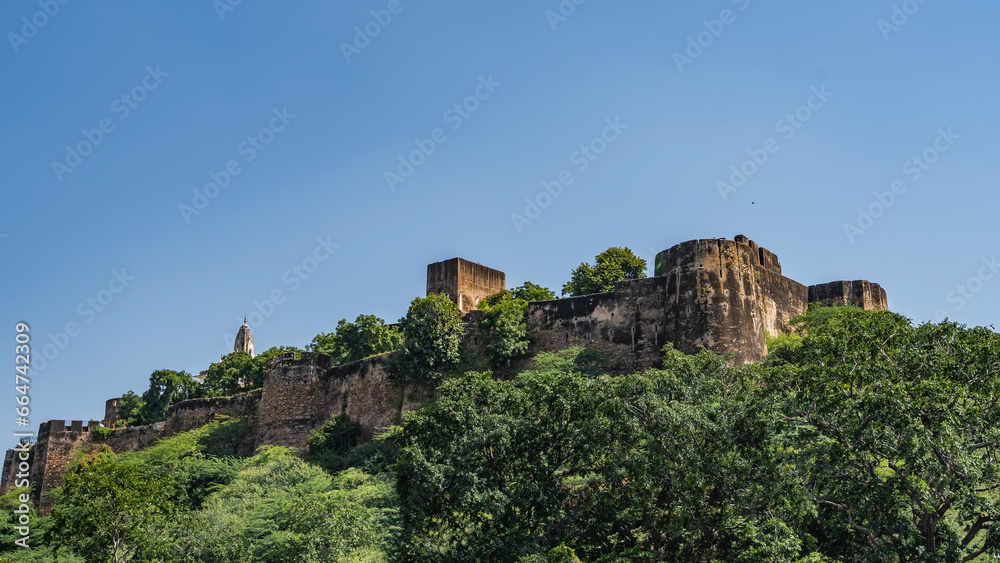 An ancient fortress wall on the crest of a mountain. Weathered mossy towers against the blue sky. Lush green vegetation on the hillside. India. Jaipur.