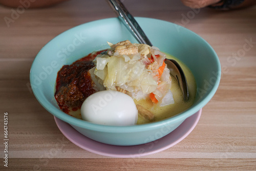 A bowl of “Lontong” or rice cake in coconut gravy with tumeric, chilli, and vegetables with some shadow and selective focus. photo
