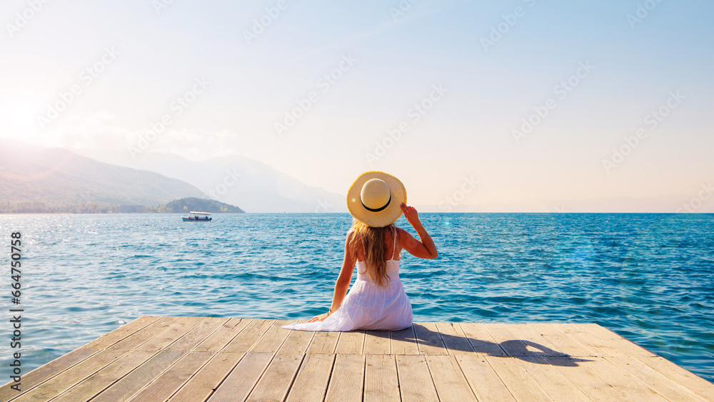 Woman in white dress and hat relaxing in front of the sea at sunset