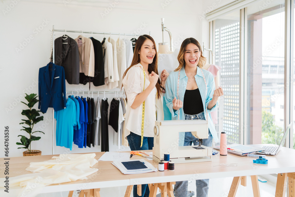 Asian female fashion designer or tailor with assistance in a happy, success and victory mood. Dressmaker working and designing new fashion collections for customers in an atelier tailor workshop.