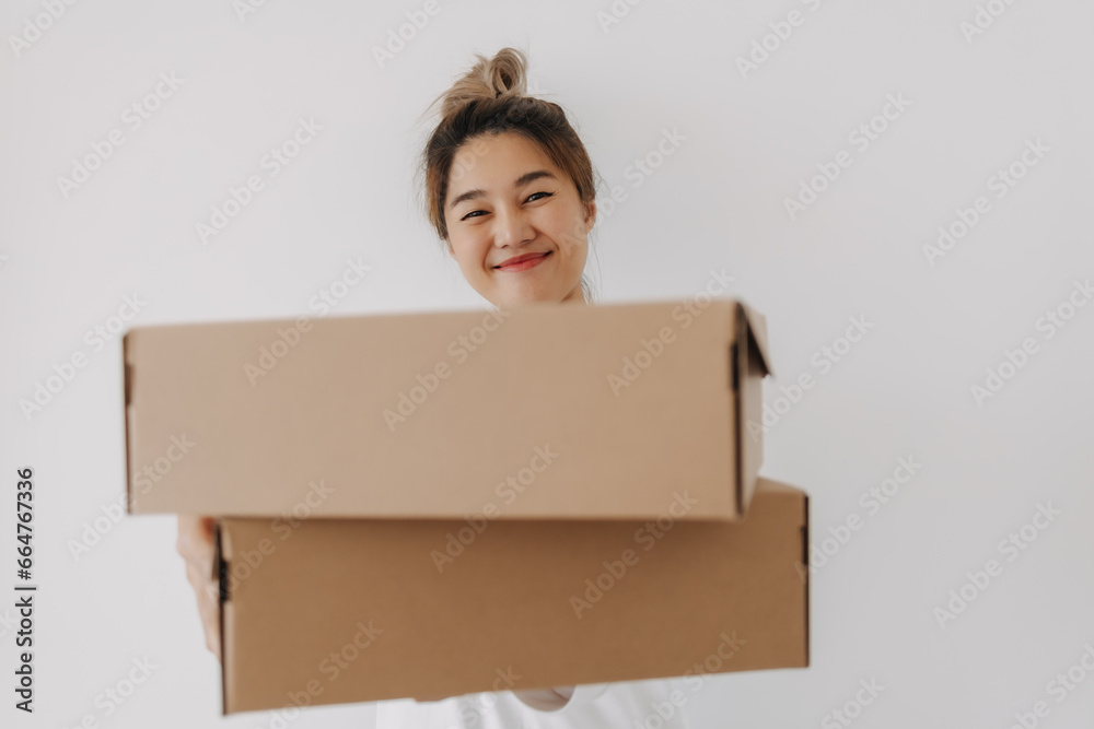 Asian Thai woman holding two parcel brown boxes, deliver and offer gift to someone, smiling and looking the camera isolated on white wall in winter. Asian Thai woman holding two parcel brown boxes, deliver and offer gift to someone, smiling and looking the camera isolated on white wall in winter.