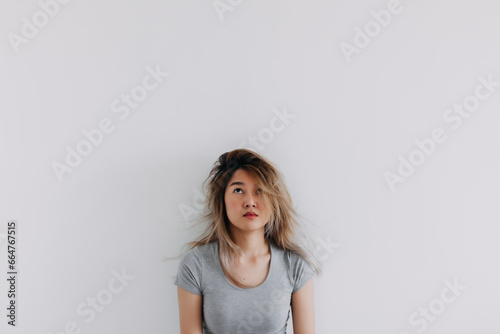 Asian Thai woman wear grey bored face, messy hair, thinking something while looking above at empty space, isolated on white background wall. photo