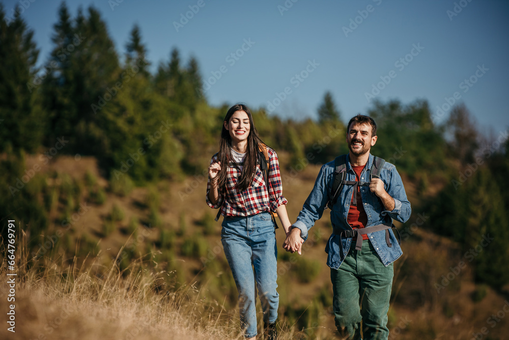 A loving couple of different ethnicities, embracing the great outdoors, cheerfully trekking upwards on a picturesque hill on a radiant, sunny day