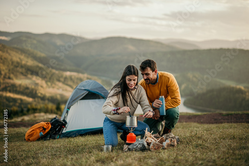 Two people bond over a campfire on a hill, savoring the sight of a distant lake