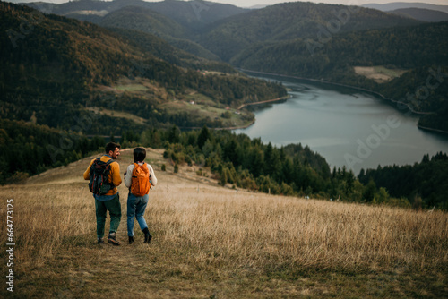 Young couple trekking with backpacks, gazing at a lake far away