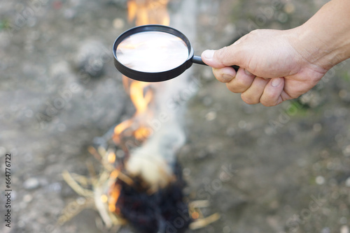 Close up hand hold magnifying glass to make fire for burning paper. Concept, Science experiment about convex lens, hold magnifying glass between the sun and tinder. Handy survival skills. 