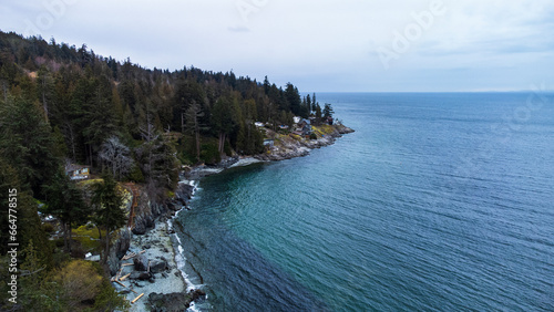 View along the coastline of Halfmoon bay. Forest trees follow the rocky coastline. Homes on the beach poke through the forest