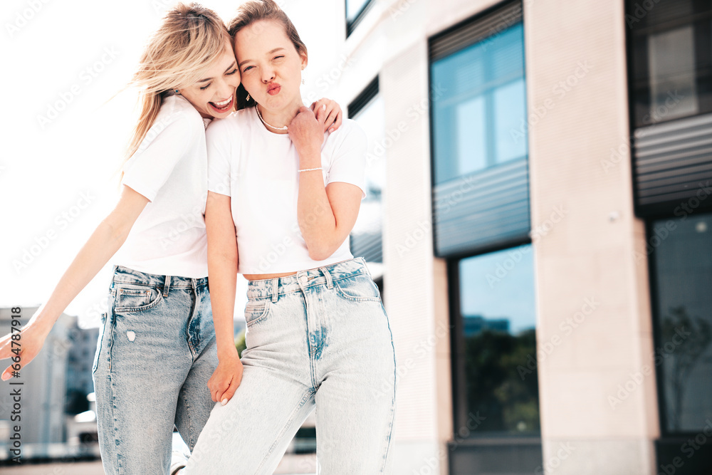 Two young beautiful smiling hipster female in trendy summer white t-shirt and jeans clothes. Carefree women posing in the street. Positive models having fun outdoors. Cheerful and happy