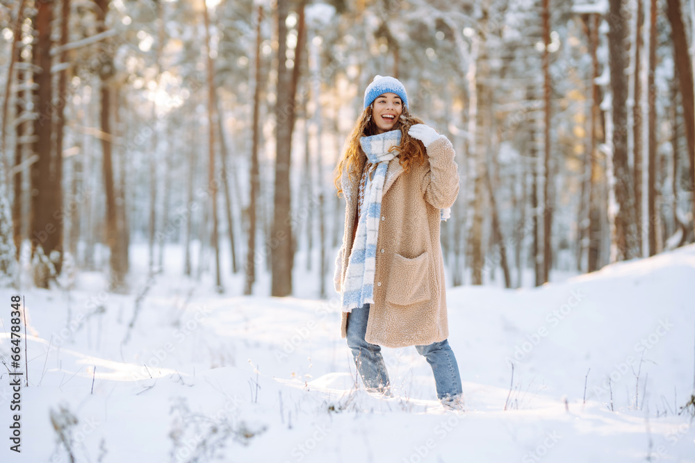 Smiling woman in a winter snow-covered park walks and plays with snow on a beautiful sunny day. Young fashionable woman in the winter forest. Walking concept, weekend. Smiling woman in a winter snow-covered park walks and plays with snow on a beautiful sunny day. Young fashionable woman in the winter forest. Walking concept, weekend.