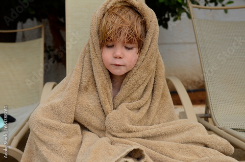 A little boy wipes himself with a towel after the pool. A child on a sun lounger, a boy frozen in the pool. Wet hair.