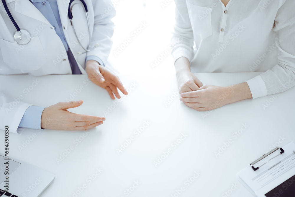 Doctor and patient discussing current health questions while sitting near of each other at the table in clinic, just hands closeup. Medicine concept