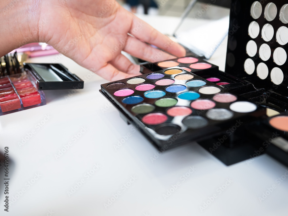 Makeup artist choose eyeshadow palette set of multicolor in small round plate, pink blush and translucent powder and color lip gloss in small case on a white cosmetic table for fashion backstage Makeup artist choose eyeshadow palette set of multicolor in small round plate, pink blush and translucent powder and color lip gloss in small case on a white cosmetic table for fashion backstage