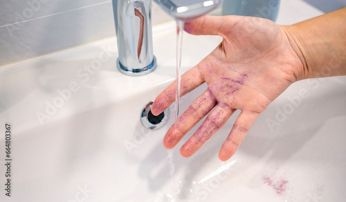 Close up of unrecognizable woman washing purple glitter of her hand into basin at bathroom and polluting clean water by toxic plastics. Concept of European Union ban use of microplastics.