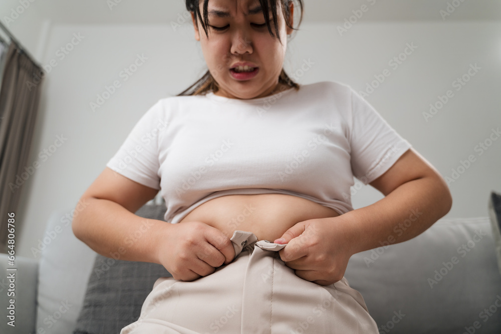 Fat chubby woman trying to wear tight pants, overweight, weight gain, Healthy and medical concept. - obrazy, fototapety, plakaty 