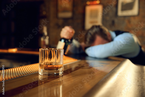 Drunk man sleeping at bar counter with focus on alcoholic drink in glass