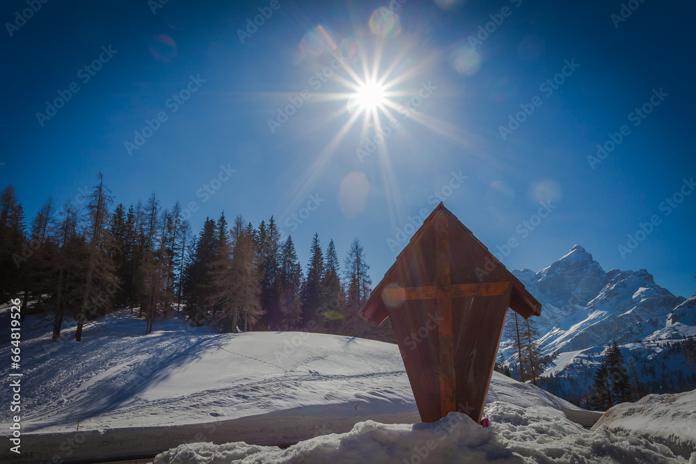 Fototapeta premium Wooden crucifix at the Staulanza Dolomite pass. Sun over Mount Civetta landscape in the background. Val di Zoldo, Belluno, Italy