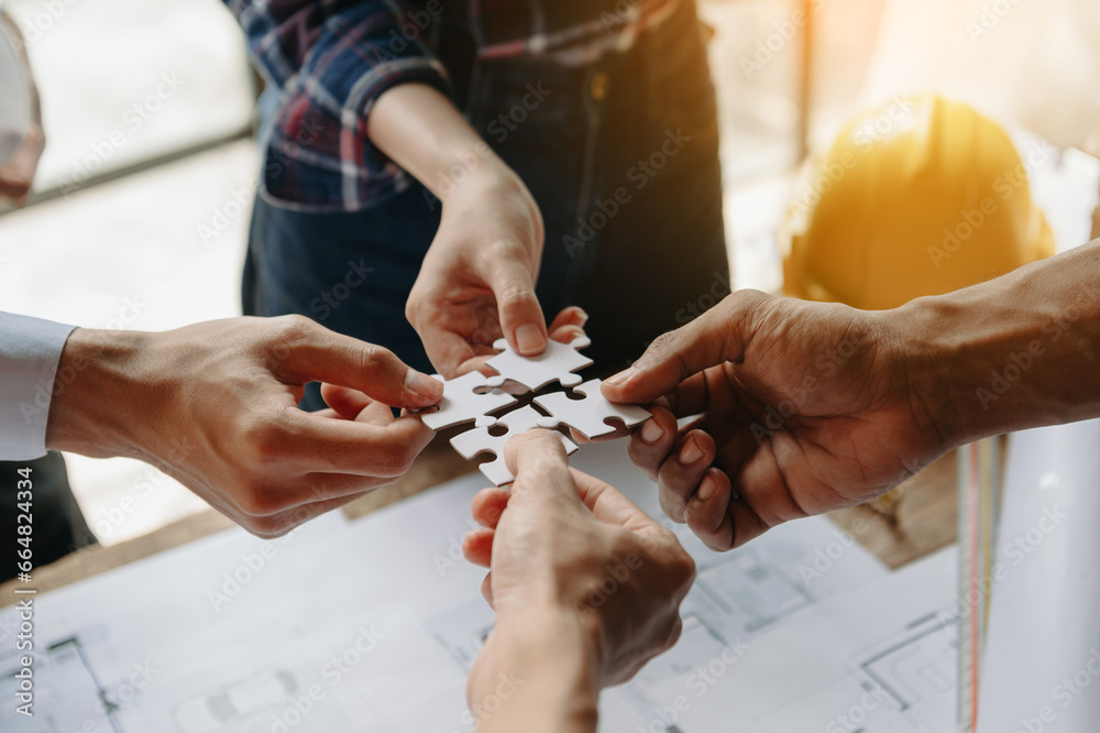 Obraz premium Construction team shake hands greeting start new project plan behind yellow helmet on desk center to consults about their building project. hand connecting jigsaw puzzle