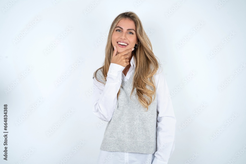 young beautiful young woman wearing formal clothing over white studio background looking confident at the camera smiling with crossed arms and hand raised on chin. Thinking positive. young beautiful young woman wearing formal clothing over white studio background looking confident at the camera smiling with crossed arms and hand raised on chin. Thinking positive.