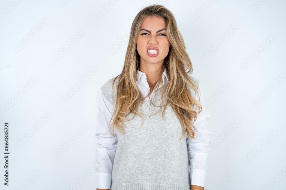 Young beautiful woman keeps teeth clenched, frowns face in dissatisfaction, irritated because of much duties.
