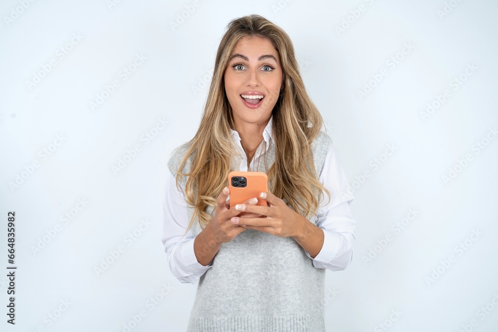 Excited Young beautiful woman holding smartphone and looking amazed to the camera after receiving good news. Excited Young beautiful woman holding smartphone and looking amazed to the camera after receiving good news.