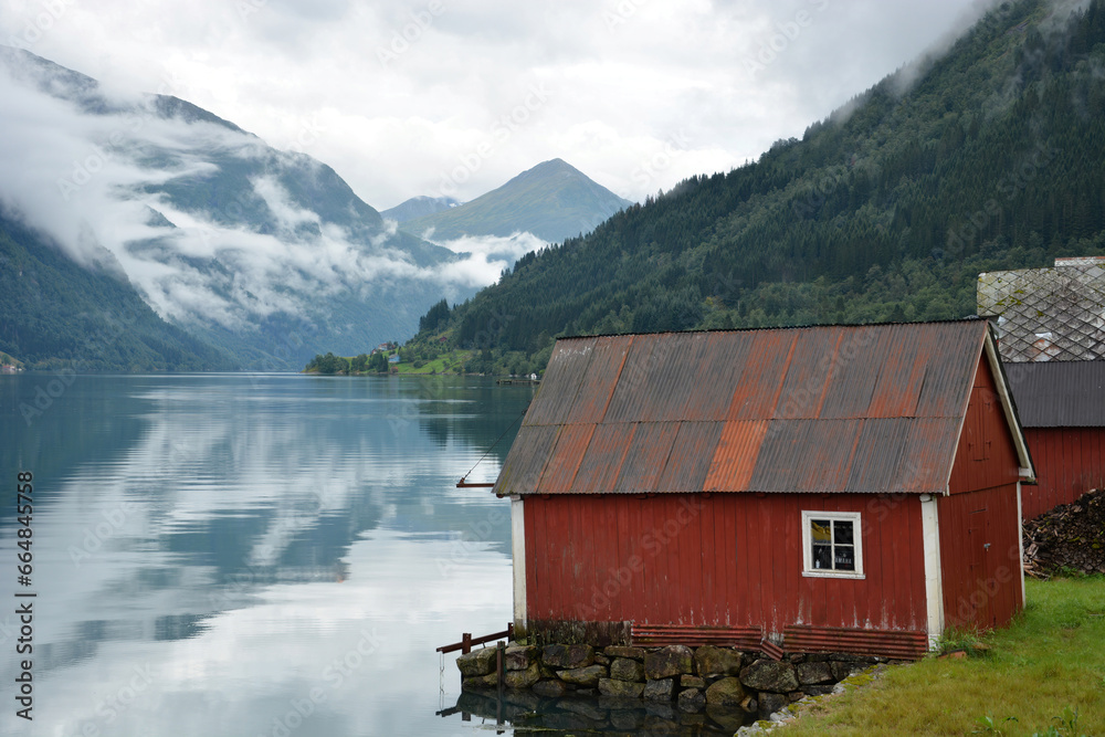 Red huts on the edge of a fjord with a mountain landscape in the background, Norway. 