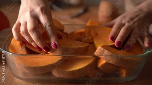 Close-up of a woman's hands placing pieces of chopped pumpkin into a glass baking dish. Pumpkin pie filling. Making a holiday pie. Vegetable dishes photo