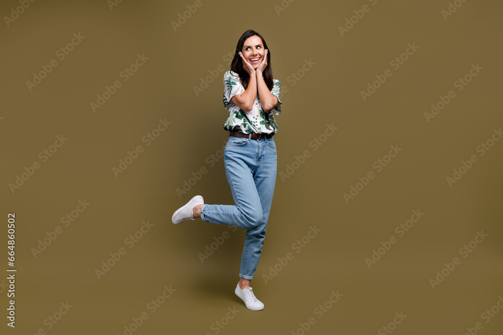 Full length photo of stunning minded person arms touch cheekbones look empty space isolated on brown color background Full length photo of stunning minded person arms touch cheekbones look empty space isolated on brown color background