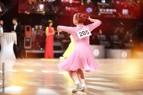 Behind the dancer - a girl dancer-athlete in a pale pink dress against the background of the stage