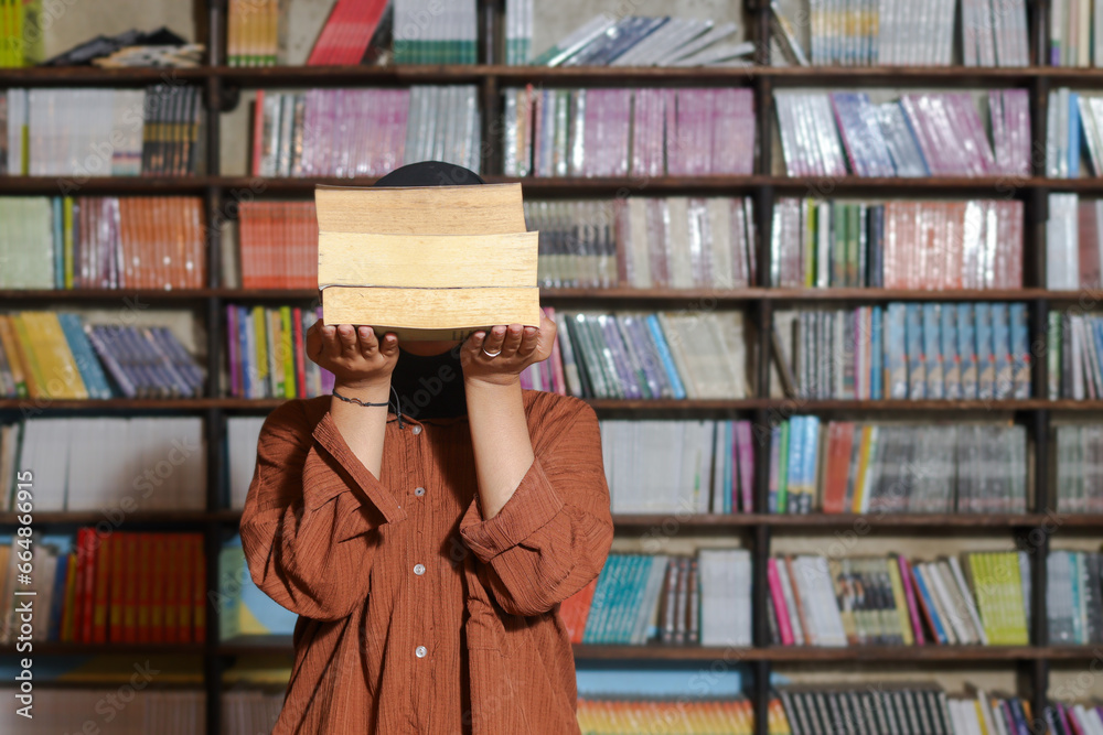 Portrait of Asian hijab woman covering her head with a pile of books in ...