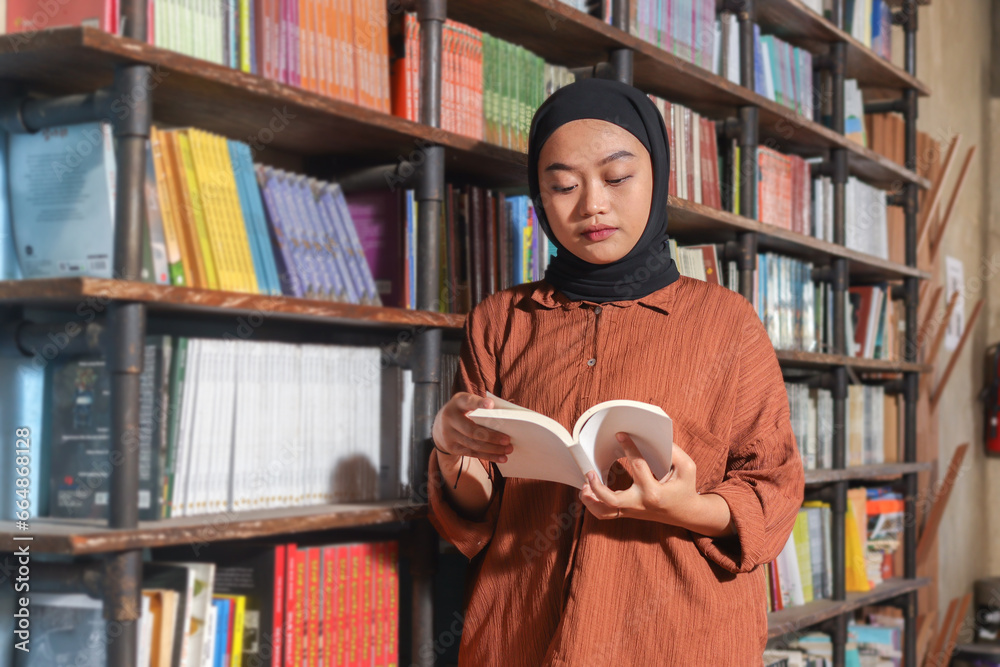 Portrait of Asian hijab woman holding book in front of library ...