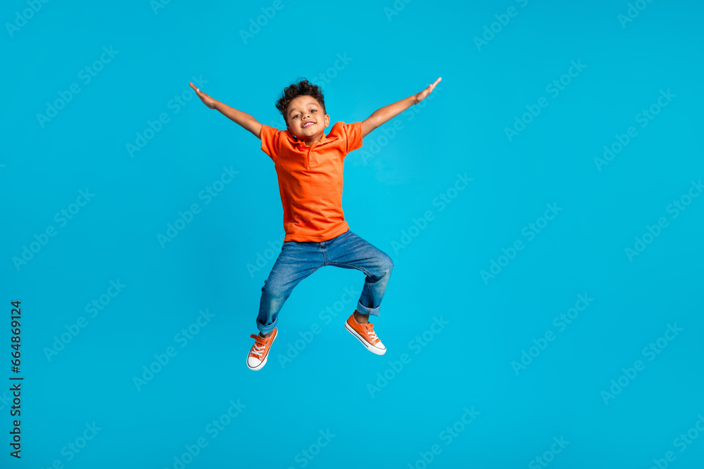 Full body cadre of jumping energetic latin small kindergarten age boy hands up positive star symbol hands isolated on blue color background