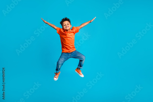 Full body cadre of jumping energetic latin small kindergarten age boy hands up positive star symbol hands isolated on blue color background photo