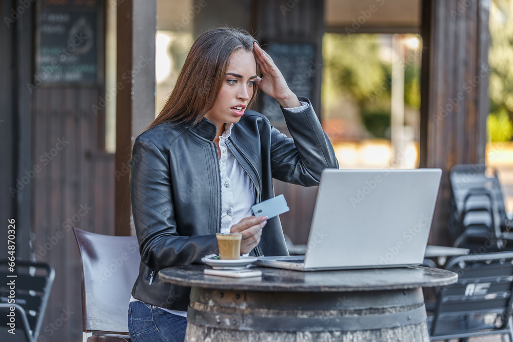 Upset woman holding credit card and looking at laptop screen Upset woman holding credit card and looking at laptop screen