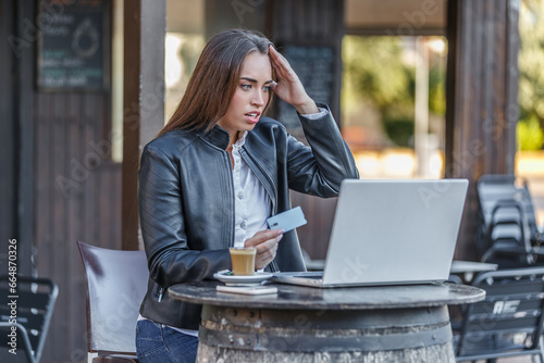 Obraz na plátně Upset woman holding credit card and looking at laptop screen