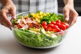 a hand placing fresh lettuce in a bowl as the first layer of a cobb salad