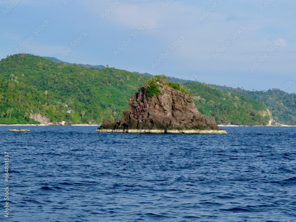 Small island in the sea. A small rocky island against the backdrop of a tropical island with beaches and jungle.