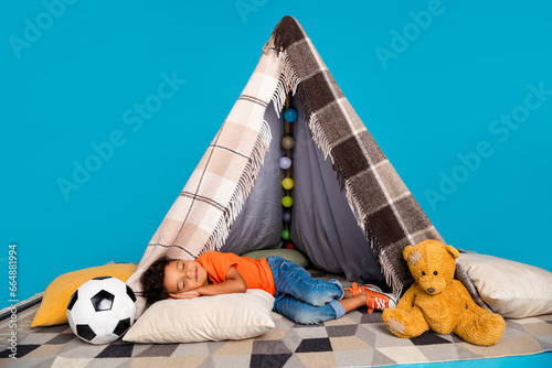 Photo of little sweet boy sleeping in diy tepee isolated over blue color background
