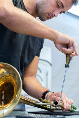 musical instrument repairman adjusting the transposer of a trombone with a screwdriver