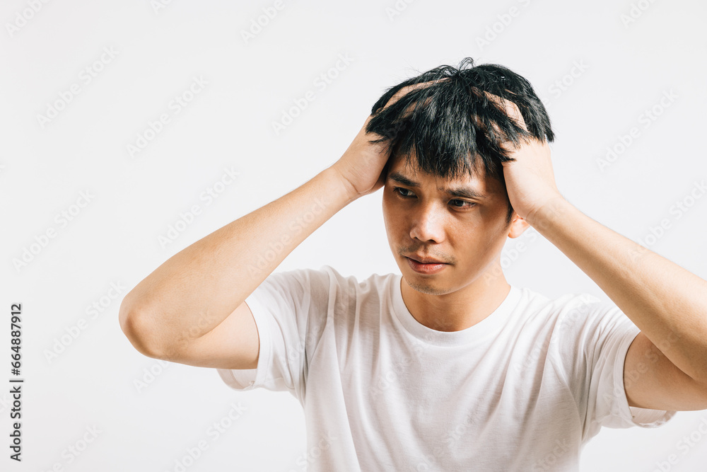 An Asian man, visibly stressed and unwell, holds his head with a pained expression, depicting the agony of a headache. Studio shot isolated on white background, conveying his suffering. An Asian man, visibly stressed and unwell, holds his head with a pained expression, depicting the agony of a headache. Studio shot isolated on white background, conveying his suffering.