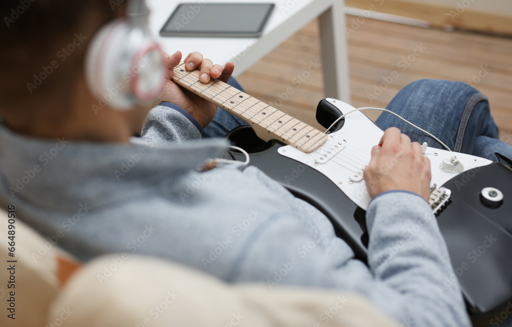 Male hands at home play and tune the electric guitar is engaged in music realizes listening enjoying music notation large concept closeup
