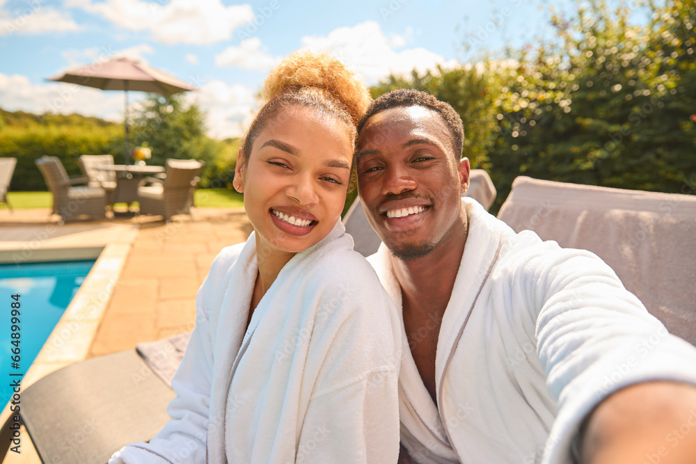 POV Shot Of Couple In Robes Outdoors By Pool On Spa Day Posing For Selfie On Mobile Phone