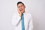 Unhealthy young Asian businessman wearing formal shirt and tie feeling dental problem and pressing sore cheek, suffering acute toothache isolated on white background
