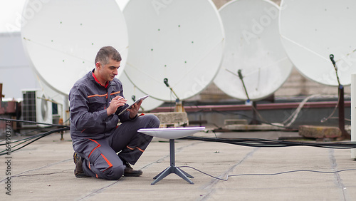 Operation and maintenance of satellite dishes under the sky, male engineer working on checking and maintaining satellite dishes. photo