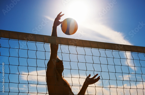 Volleyball, fitness and man at beach with ball serve, energy or freedom on blue sky background. Seaside, sports or male player with handball in nature for cardio, workout or athletic game performance photo