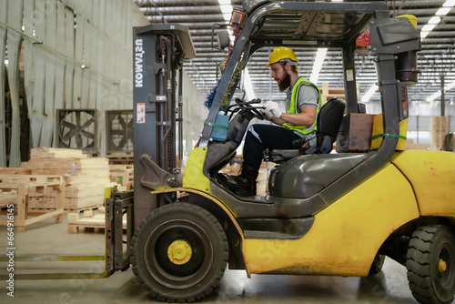 Warehouse worker wears safety helmet driving forklift truck in pallet factory. Skilled male logistic engineer working in shipping storage manufacturing lifting, moving and unloading cargo for delivery © Nassorn