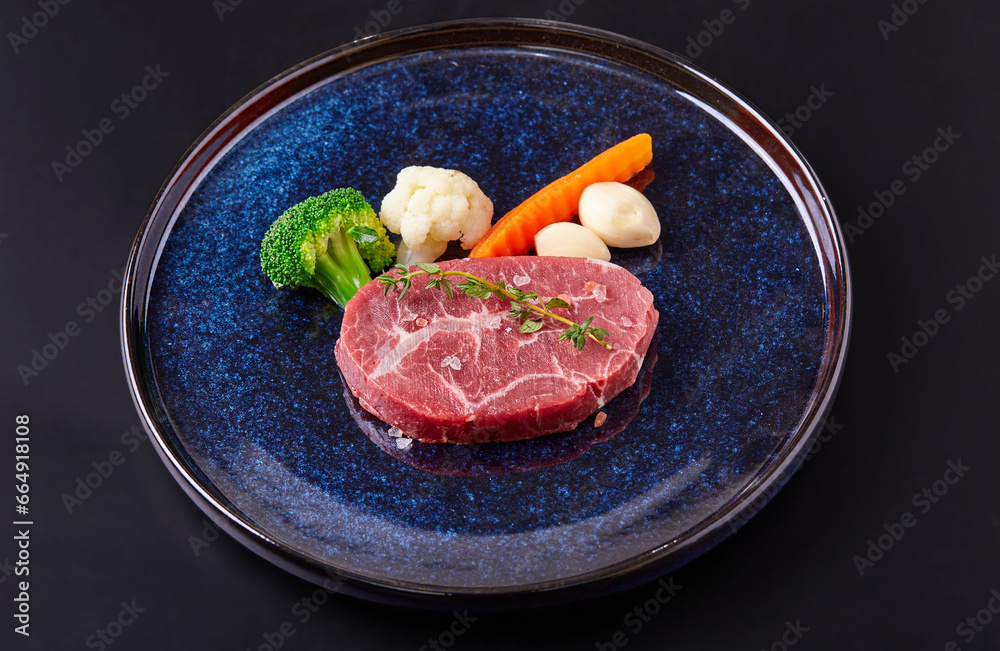 Raw Paleron (Oyster blade) with vegetable (Broccoli, cauliflower, garlic) top with Himalayan salt and thyme leaves on plate isolated on black background. Prepare beef and vegetables for cooking. Raw Paleron (Oyster blade) with vegetable (Broccoli, cauliflower, garlic) top with Himalayan salt and thyme leaves on plate isolated on black background. Prepare beef and vegetables for cooking.