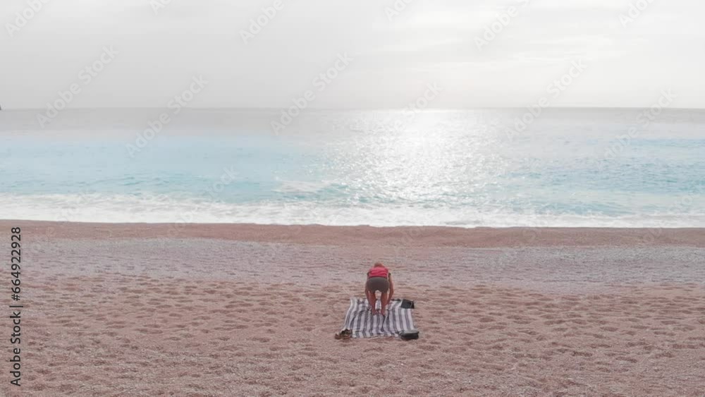 Slow motion: aerial view of woman performing yoga exercises on a beautiful empty beach in Greece. Dramatic coastline scenic bay rocky cliffs in the Ionian island, Port Katsiki, Lefkada.