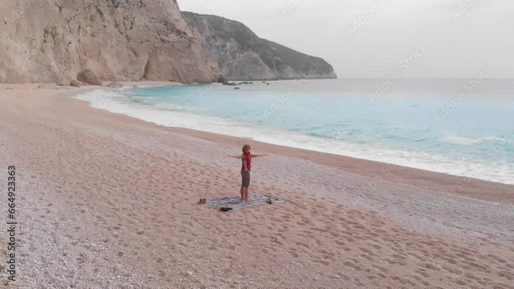 Slow motion: aerial view of woman performing yoga exercises on a beautiful empty beach in Greece. Dramatic coastline scenic bay rocky cliffs in the Ionian island, Port Katsiki, Lefkada. Slow motion: aerial view of woman performing yoga exercises on a beautiful empty beach in Greece. Dramatic coastline scenic bay rocky cliffs in the Ionian island, Port Katsiki, Lefkada.