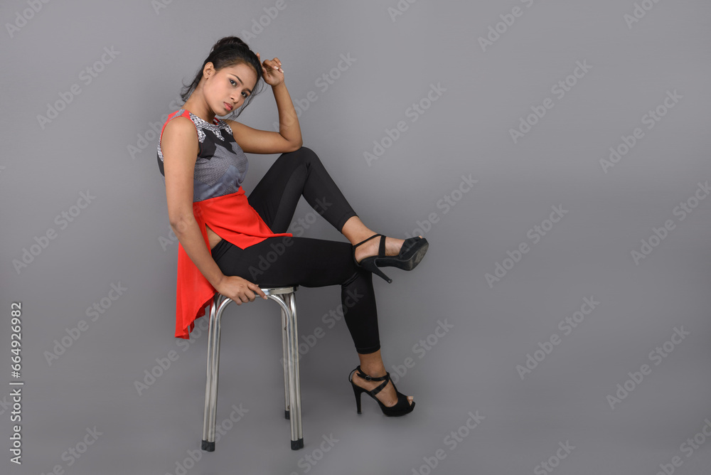 Studio shot of a young, beautiful Indian female model in casual wear wearing red and grey designer top and black jeans against white background. Female model. Fashion Portrait. Studio shot of a young, beautiful Indian female model in casual wear wearing red and grey designer top and black jeans against white background. Female model. Fashion Portrait.