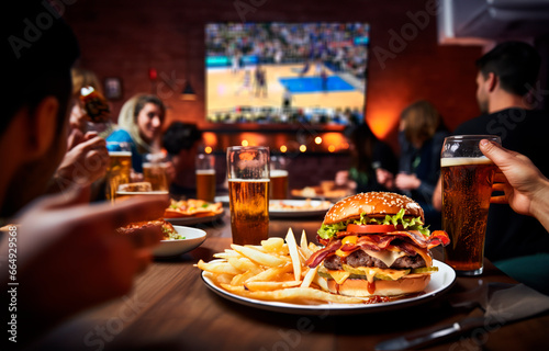 Beer, Basketball, and Big Burgers: Friends Enjoying the Game on TV with Tasty Bites in a Fun and Exciting Social Gathering.

